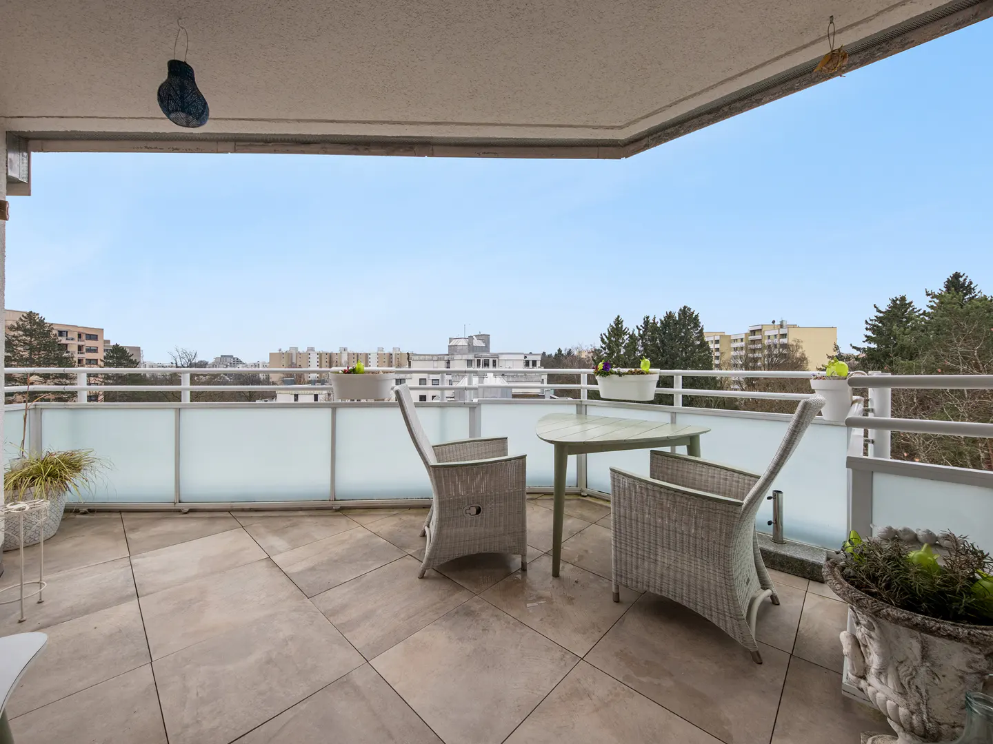 Balcony with two wicker chairs and a table overlooking a city skyline under a blue sky.