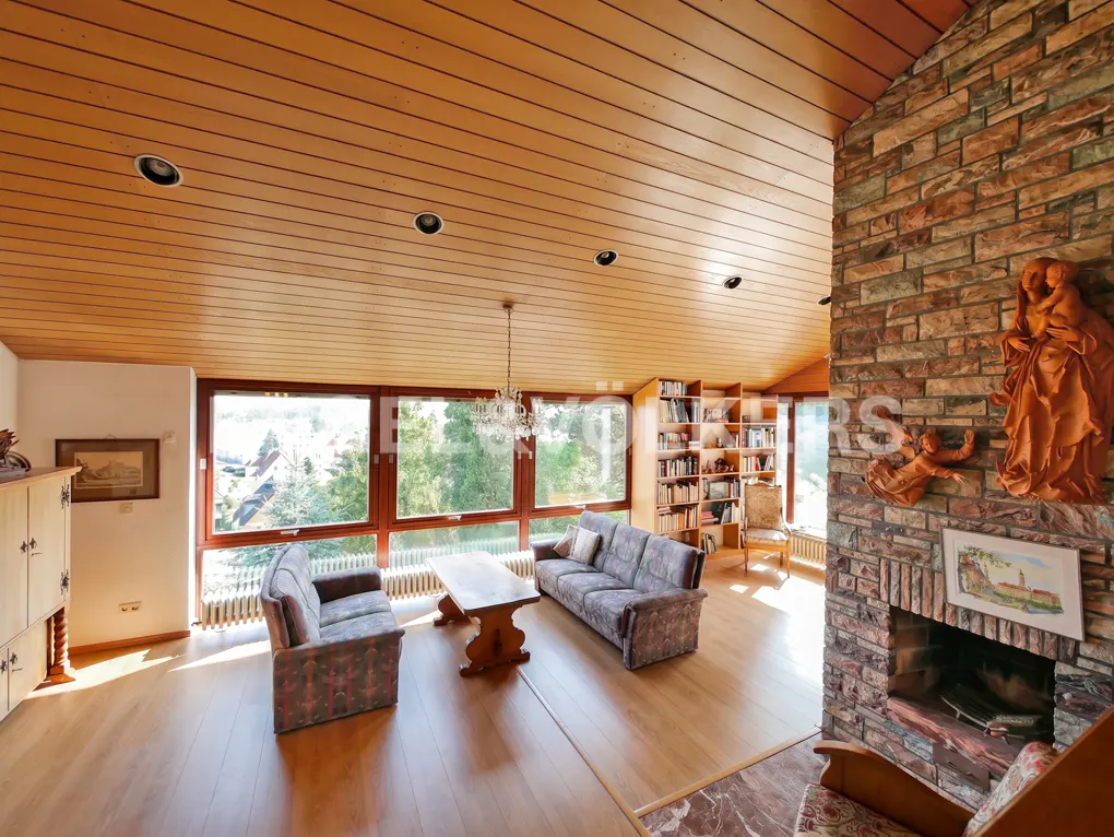 A living room with wood floors, a brick fireplace, sofas, and large windows.