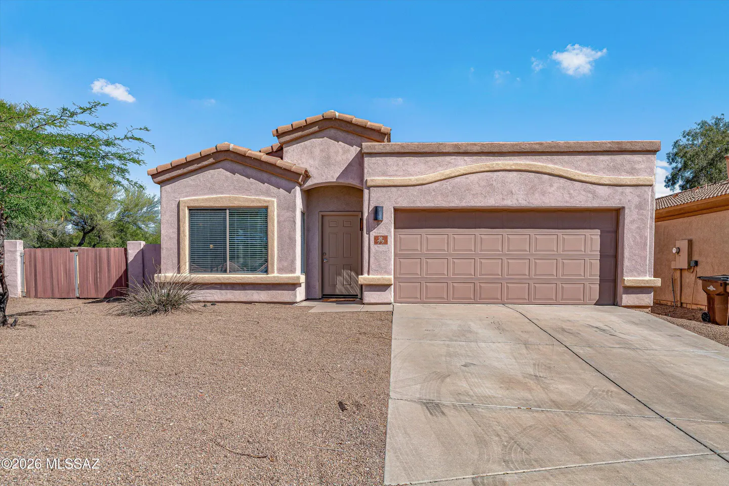 A single-story stucco house with a brown garage door and a gravel front yard under a blue sky.