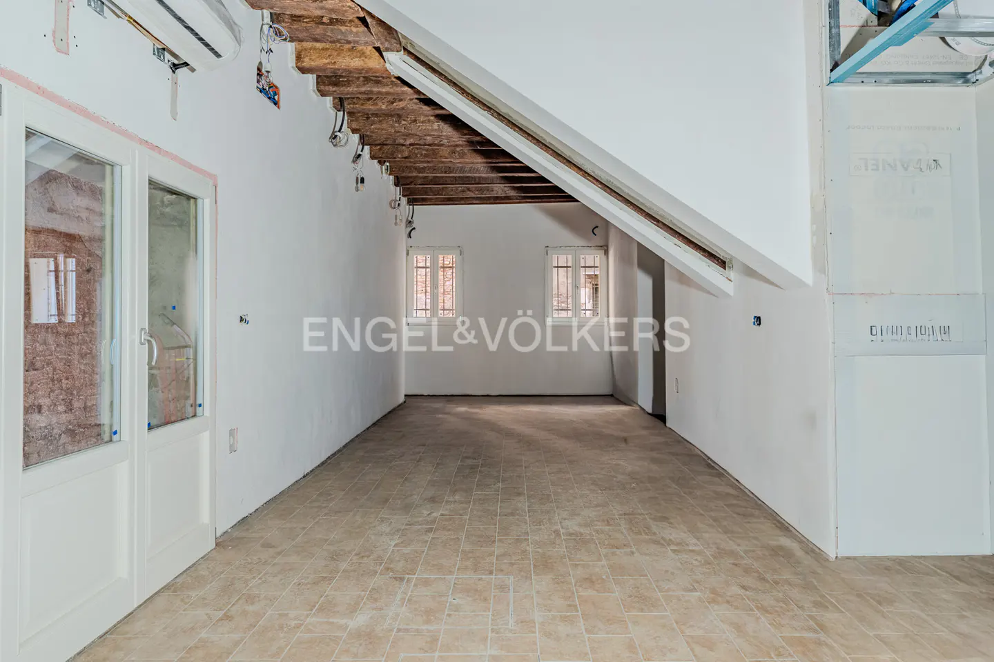 Unfinished attic room with white walls, tile floor, and exposed wood beams. Two windows are visible in the back wall.