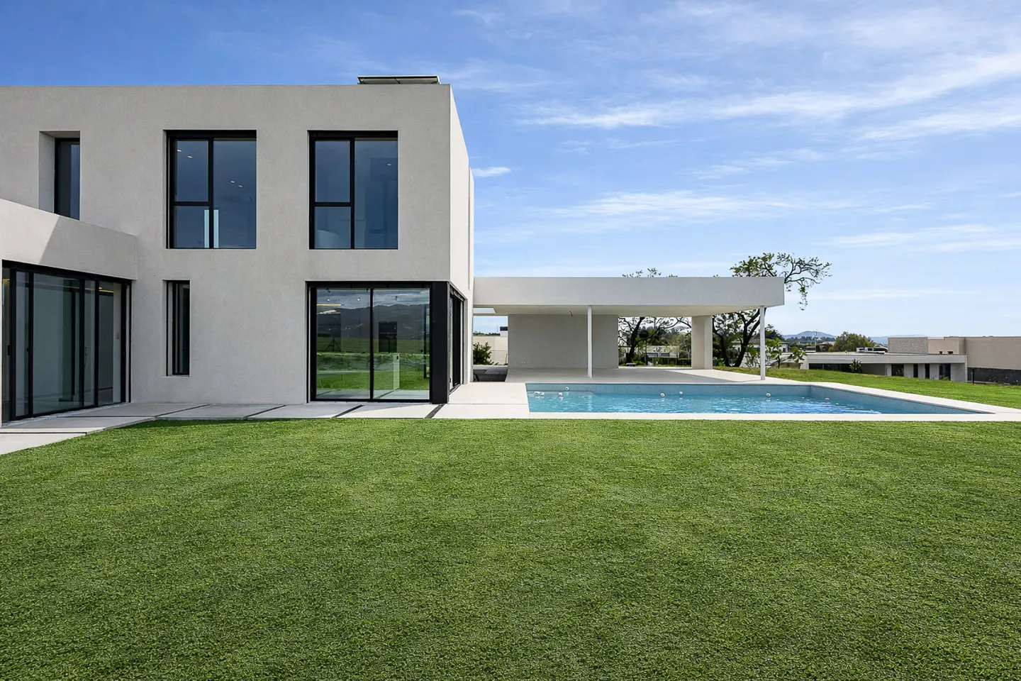 Modern white house with black framed windows, a pool, and green lawn under a blue sky.