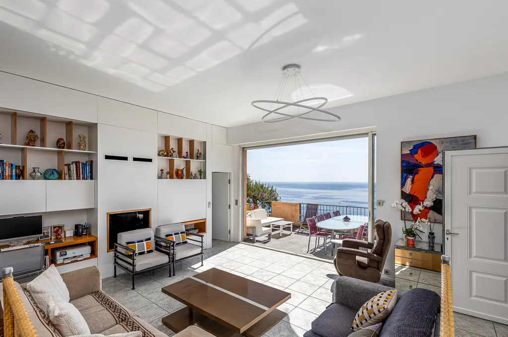Bright living room with white walls, built-in shelves, and a large sliding glass door leading to a patio with ocean views.