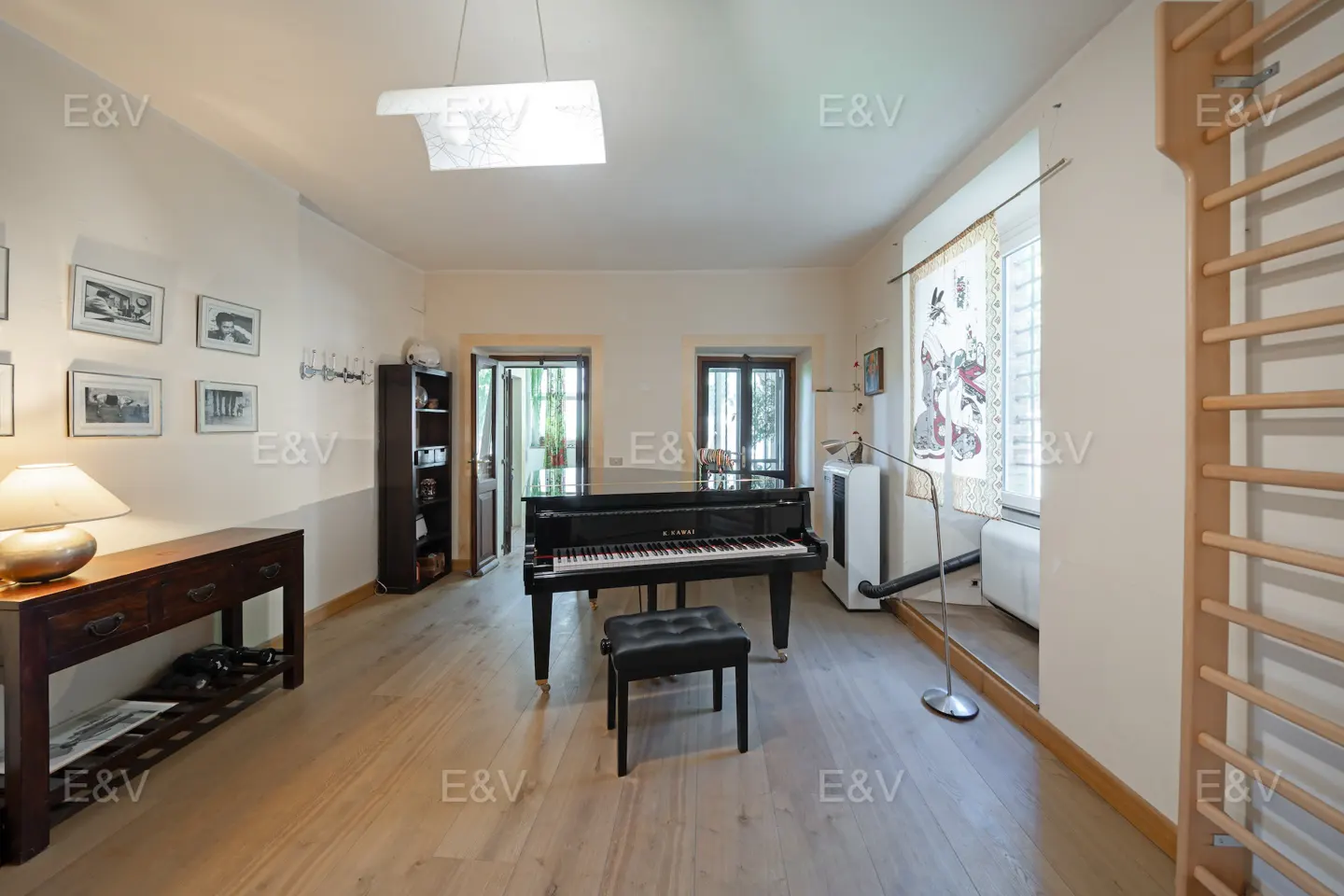 A bright room with a black piano, stool, wooden floors, and wall bars.