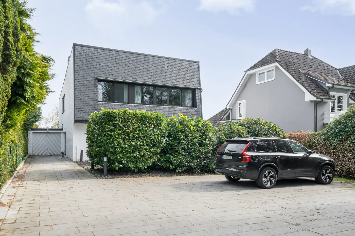 Exterior view of a modern two-story house with a gray slate roof, white walls, and a black SUV parked in the driveway.