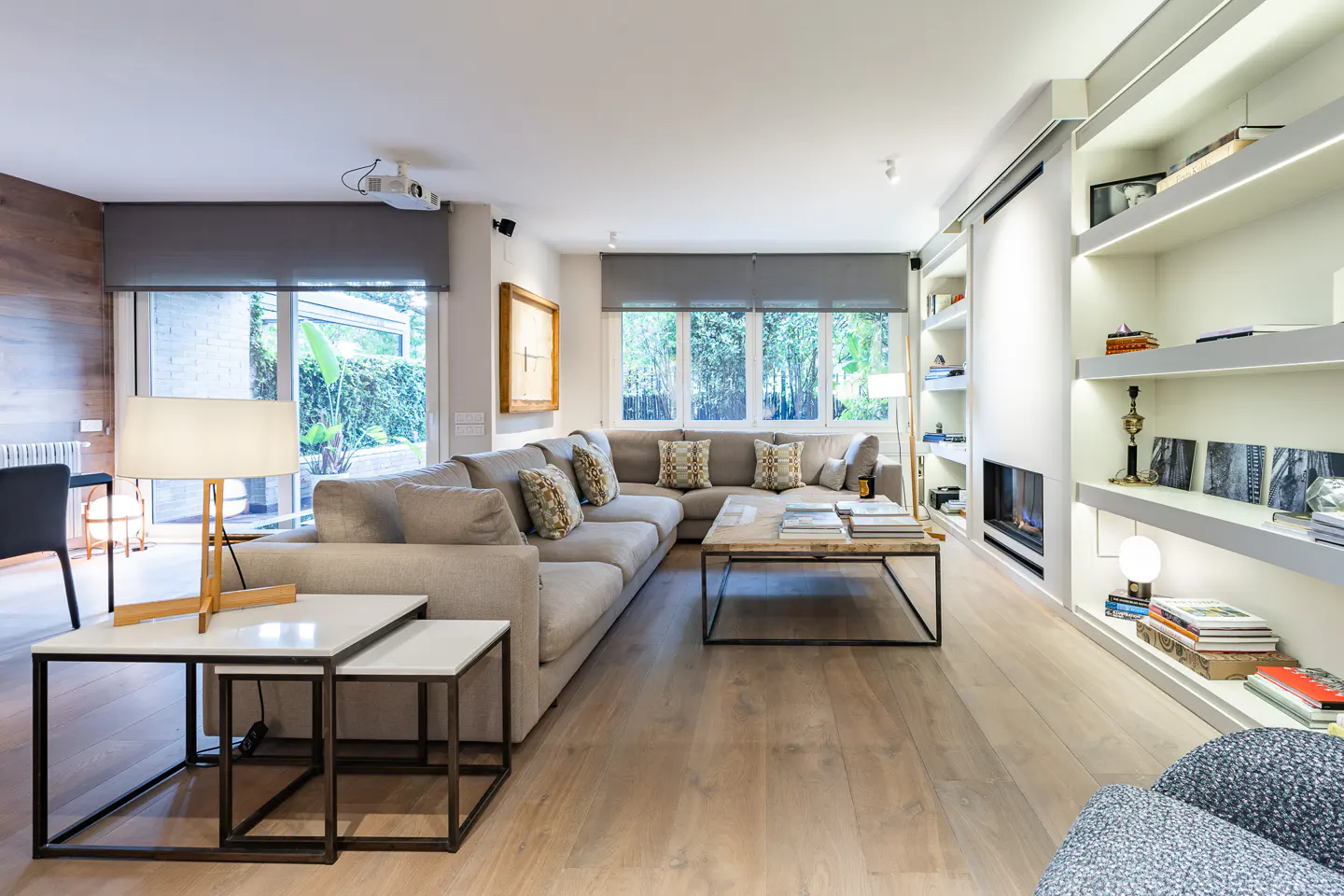 Bright living room with a large gray sectional sofa, wooden floors, and built-in white shelves with a fireplace.