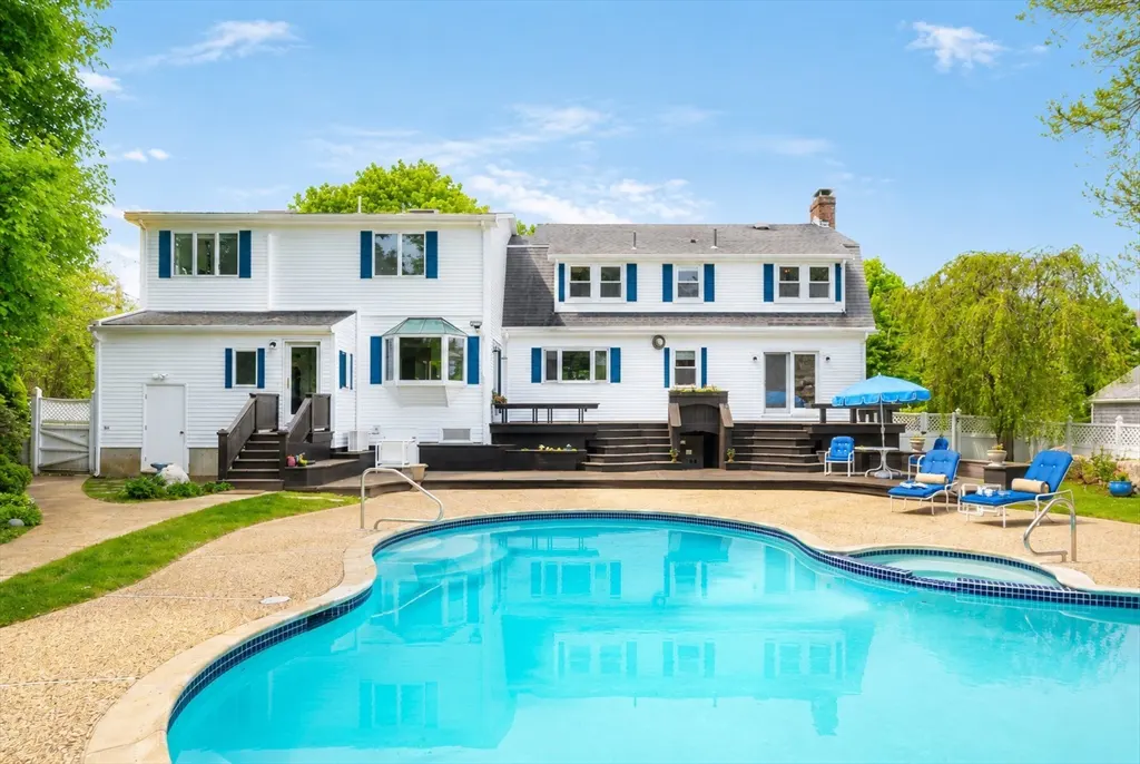 Back view of a two-story white house with blue shutters and a kidney-shaped pool.