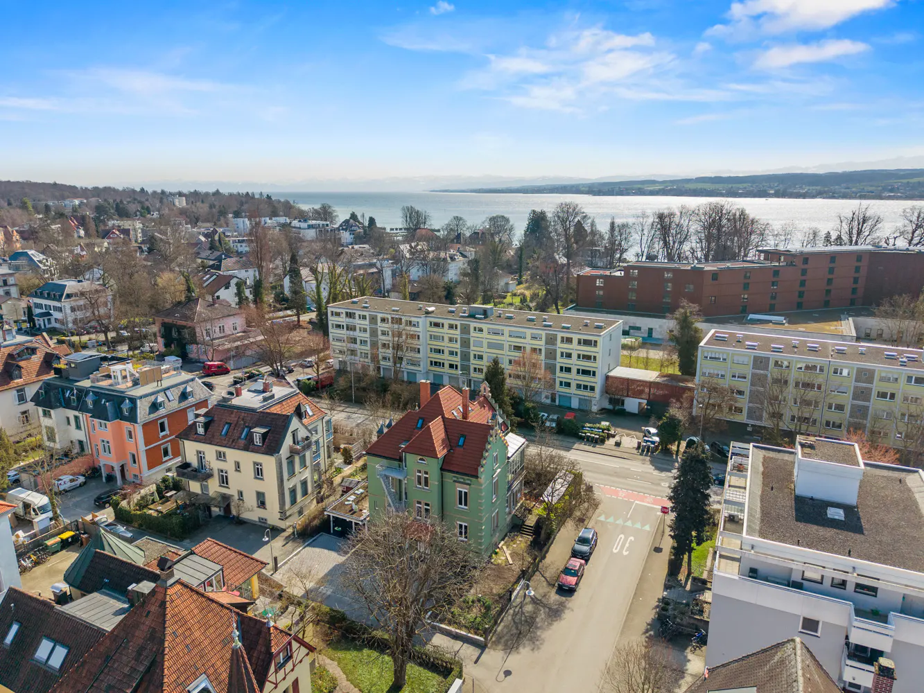 Aerial view of a European town with colorful houses, apartments, and a lake in the background under a blue sky.