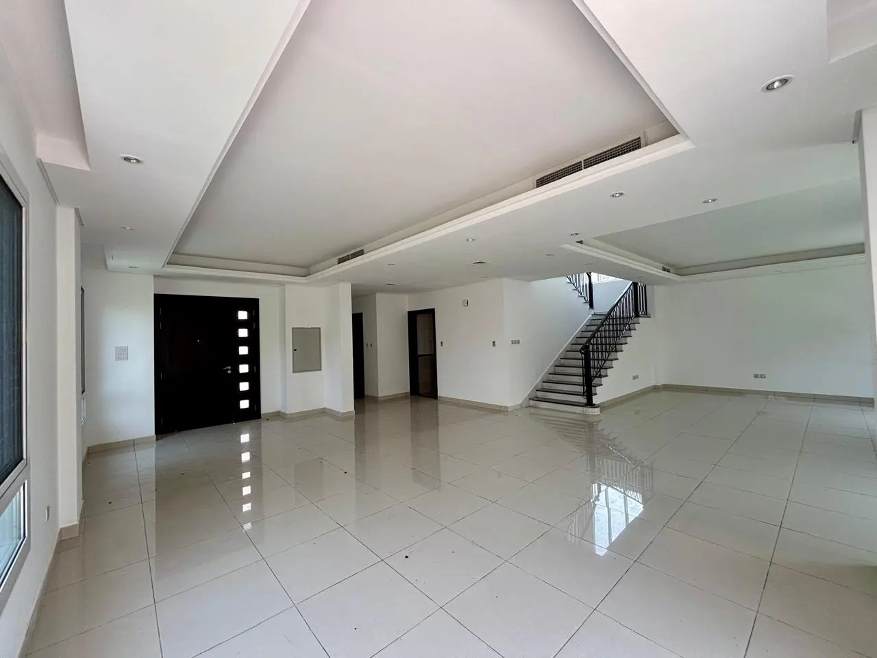 Bright, empty living room with white tile floors, white walls, and a black front door. Stairs lead to the second floor.