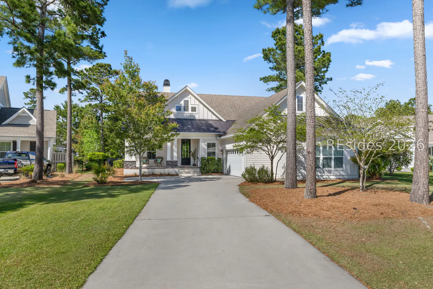 Exterior view of a white, single-story house with a gray roof and a concrete driveway, surrounded by green grass and trees.