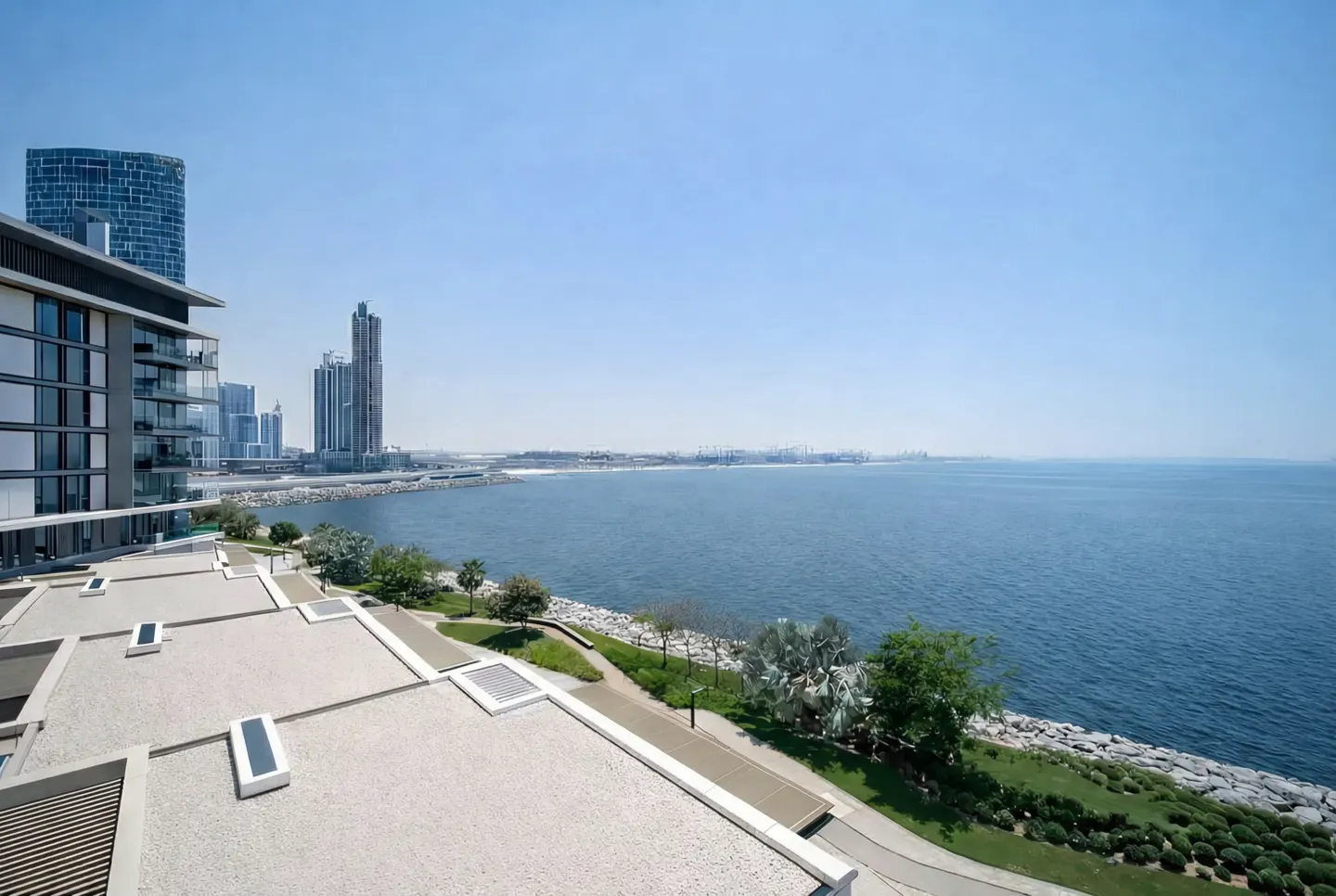 View from a building overlooking the sea, with a park, and city buildings in the background.