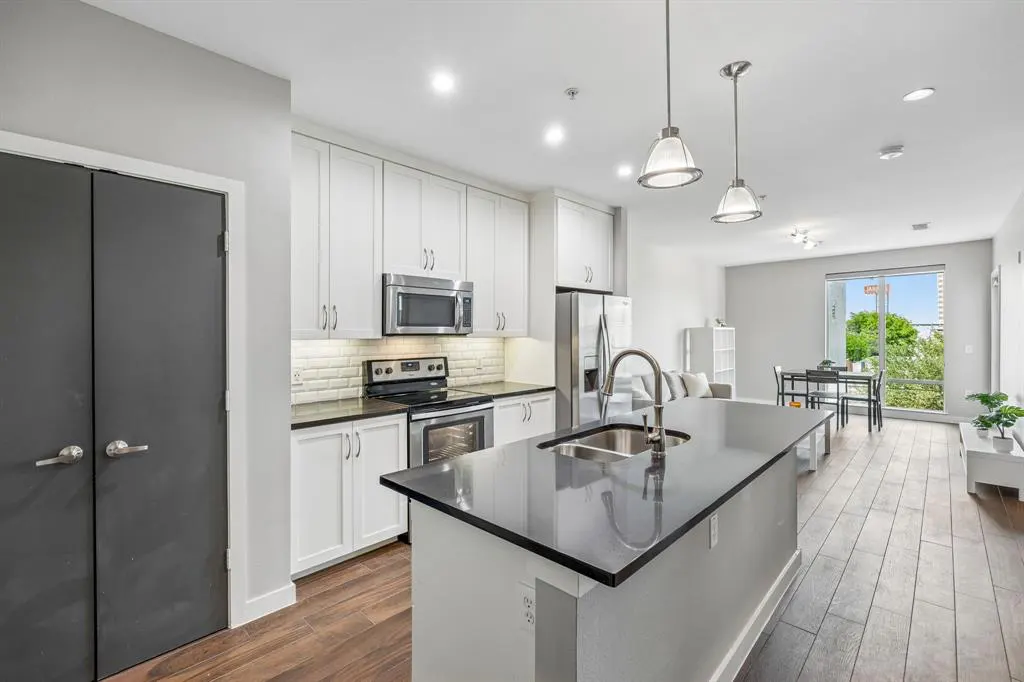 A modern kitchen with white cabinets, stainless steel appliances, and a black countertop island. Hardwood floors and gray walls complete the space.