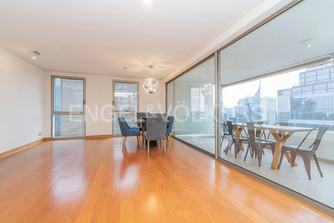 Modern dining room with hardwood floors, a glass chandelier, and a balcony featuring a dining set overlooking city buildings.