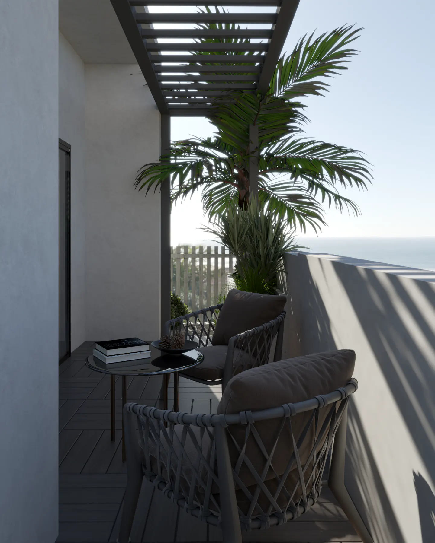 Outdoor patio with gray wicker chairs, a small table with books, and a palm tree under a pergola, overlooking the ocean.