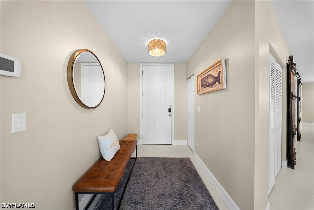 Beige entryway with a brown leather bench, round mirror, and gray rug. A white front door is centered, with a whale art piece on the right wall.