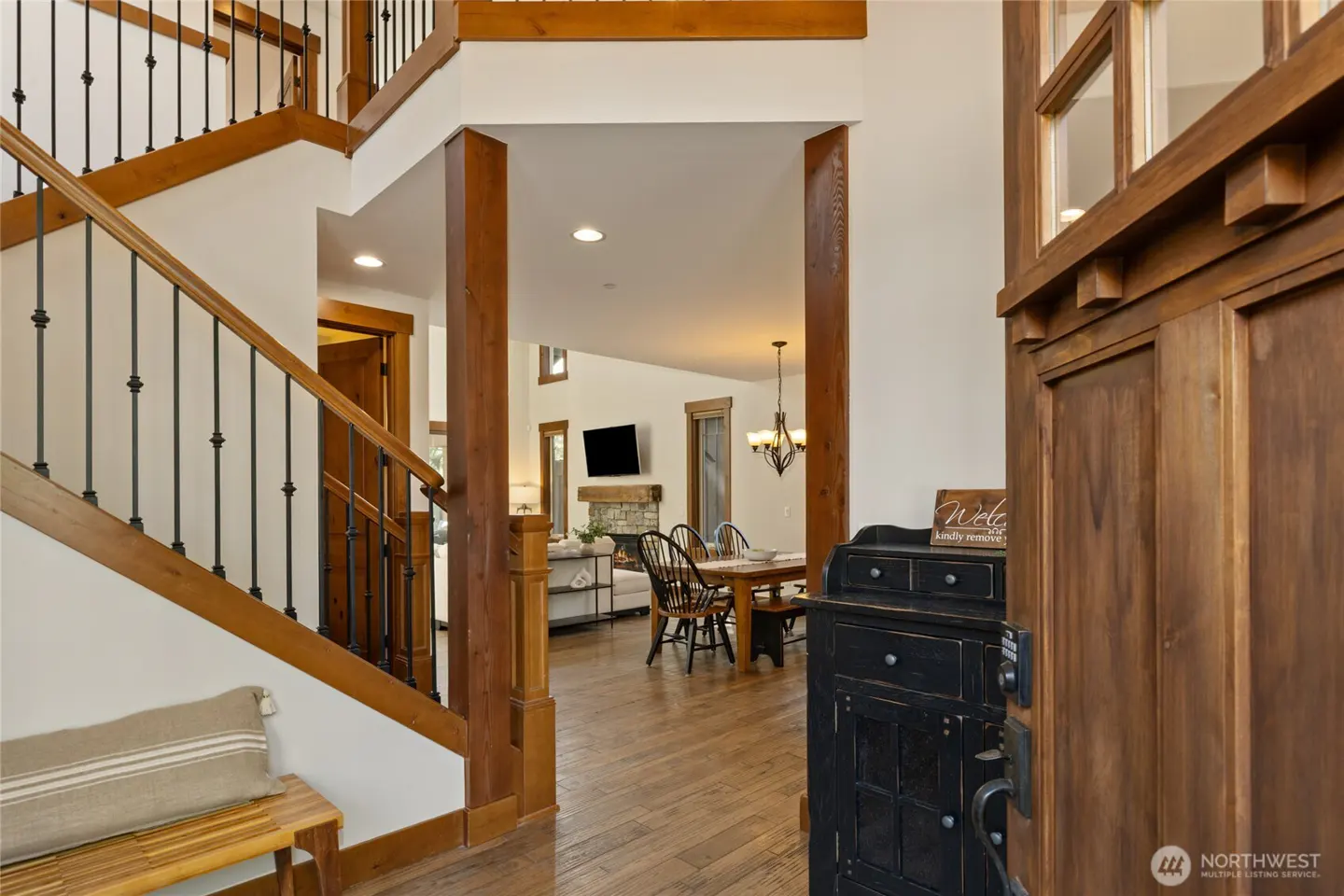Open wood front door reveals a home's interior: staircase with black railing, dining table, and living room with a stone fireplace.