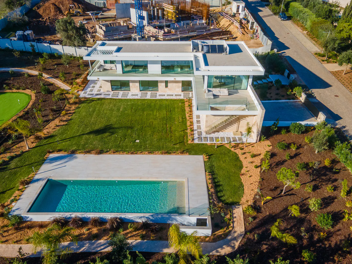 Aerial view of a modern white house with a pool, green lawn, and construction in the background.