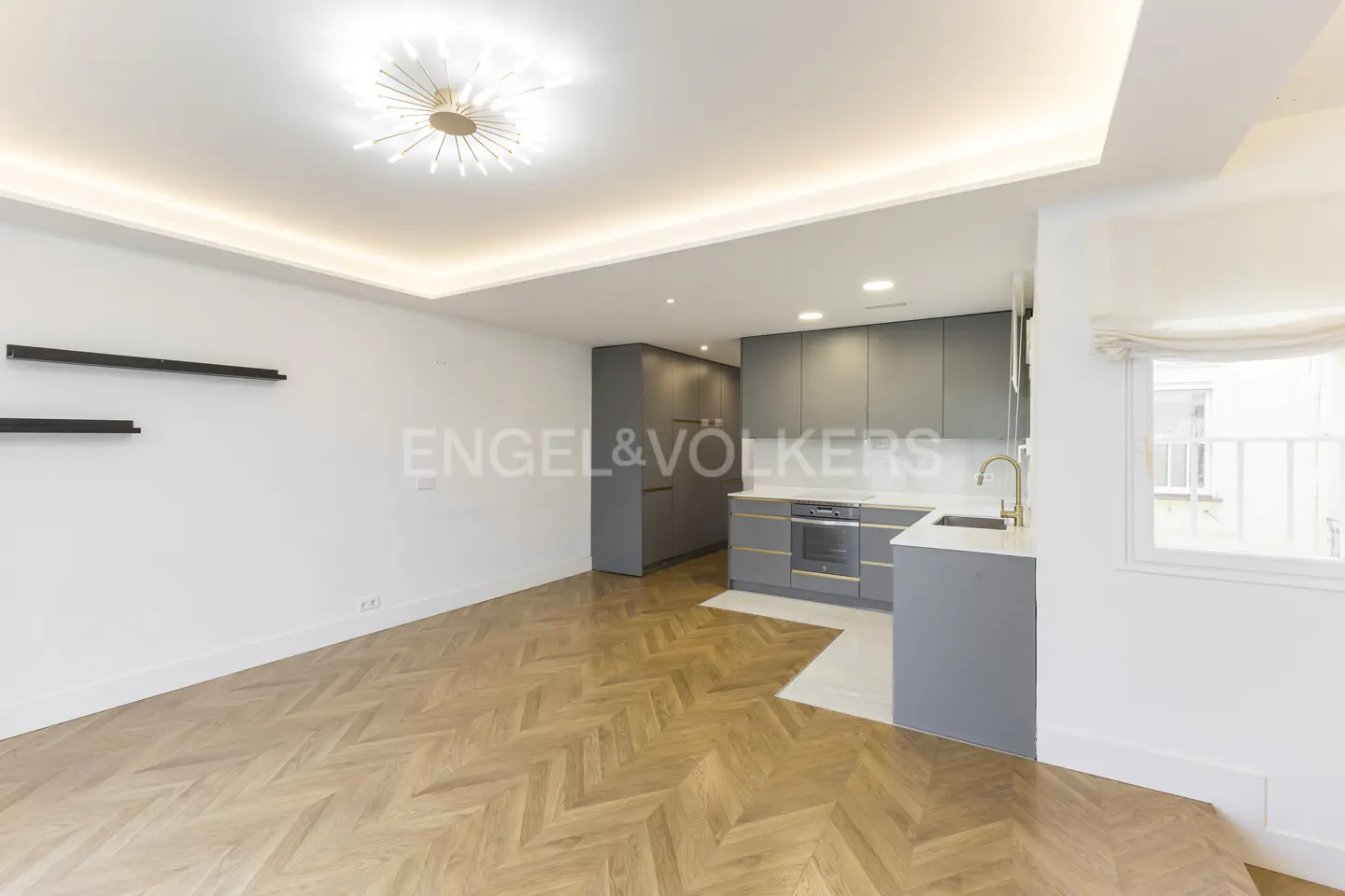 Modern open-plan kitchen with grey cabinets, herringbone wood floors, and a starburst ceiling light fixture.
