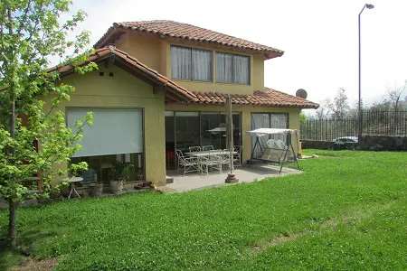 Two-story yellow house with a red tile roof, patio furniture, and a green lawn.