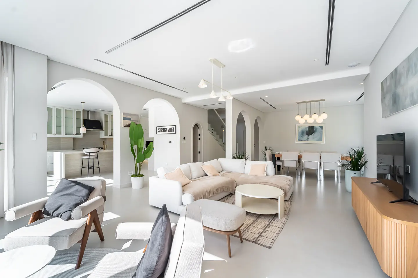 Bright, open-concept living space with white walls, arched doorways, and modern furniture. A kitchen, dining area, and lounge are visible.