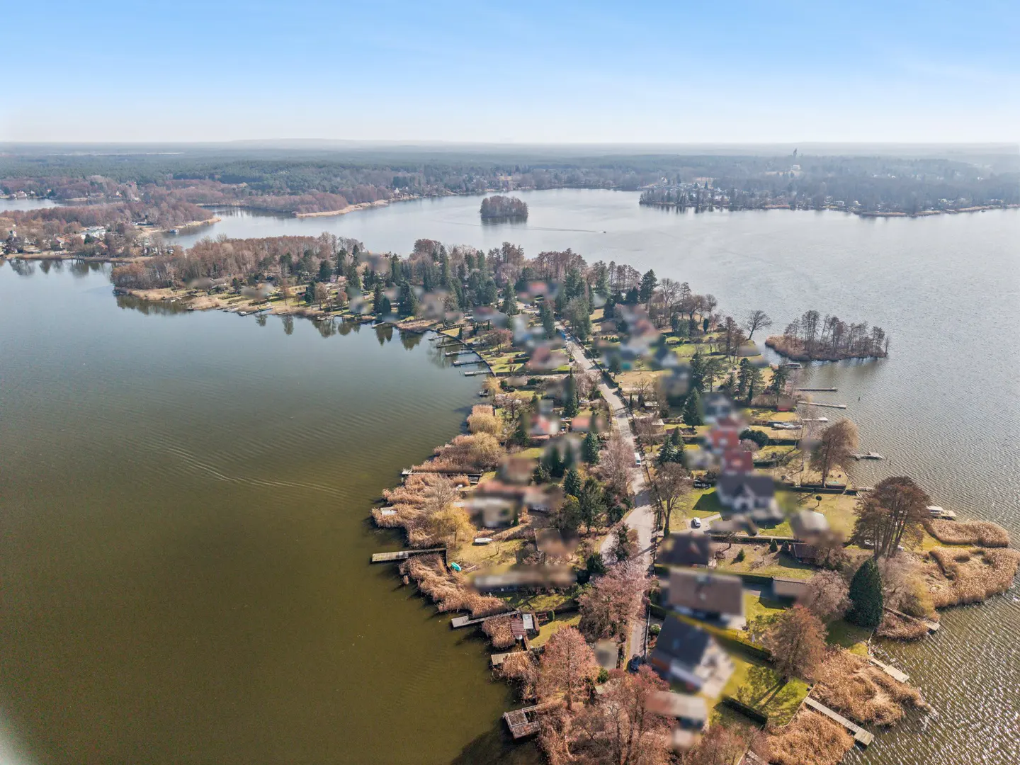 Aerial view of a peninsula with houses, trees, and docks surrounded by a lake under a clear blue sky.