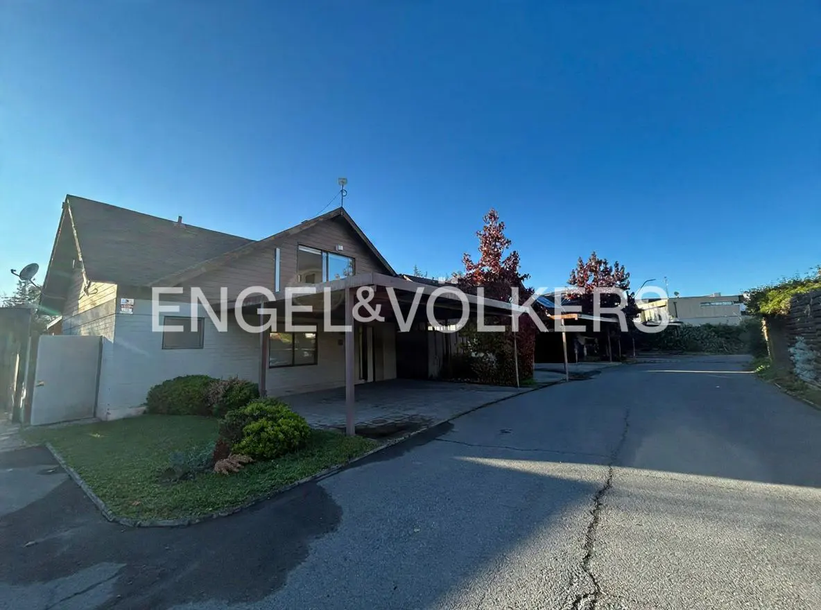 Exterior view of a brown house with a carport and the Engel & Volkers logo on the facade. Blue sky background.