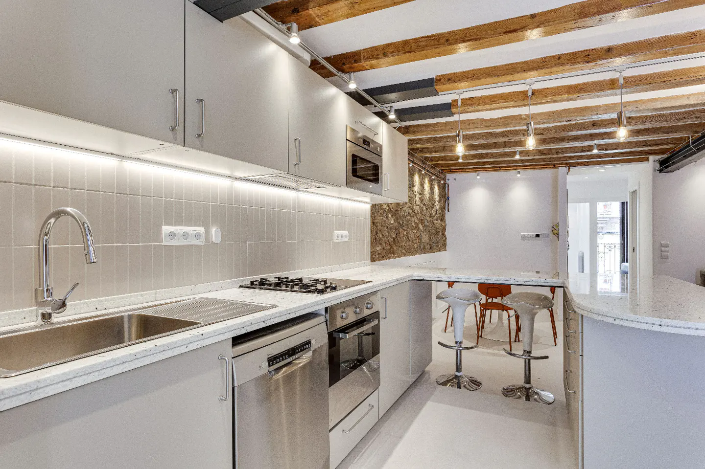 Bright kitchen with white cabinets, stainless steel appliances, and a stone accent wall. Wooden beams adorn the ceiling.