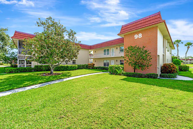 Exterior view of a two-story apartment building with red roof and green lawn under a blue sky. Building number 98 is visible.