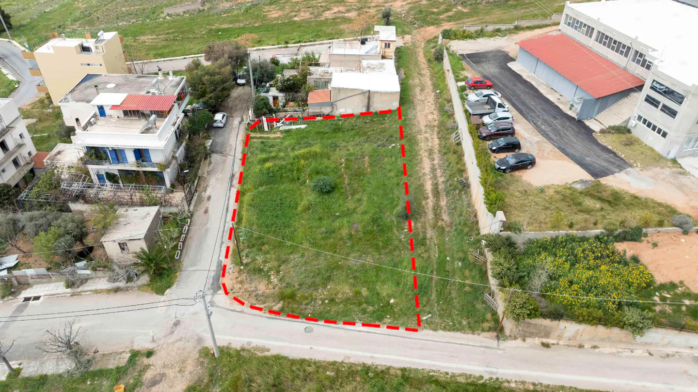 Aerial view of a vacant rectangular plot of land outlined in red, situated between residential and commercial buildings.