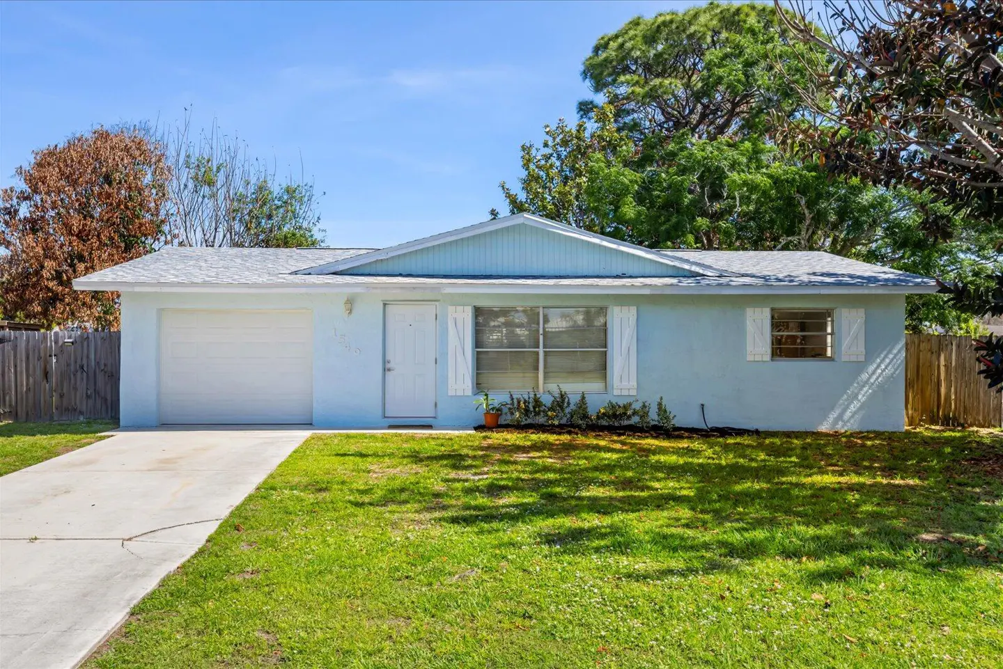A light blue single-story house with a white garage door and white trim on a sunny day.