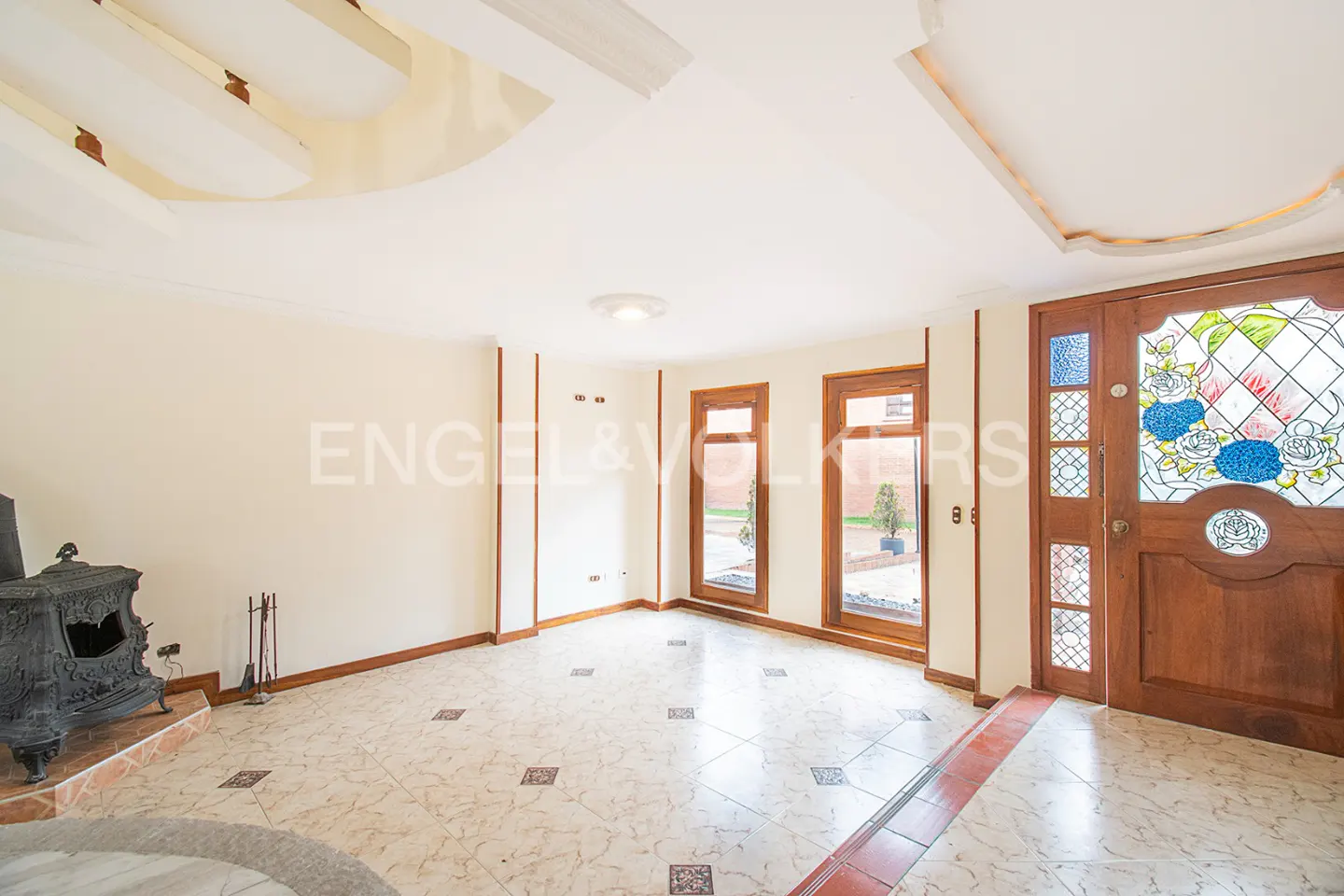 A bright living room with a wood door with stained glass, a fireplace, and tile floors.