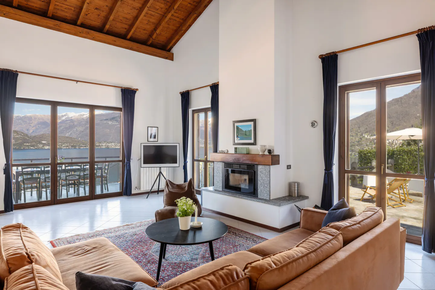Bright living room with brown leather sofas, fireplace, and large windows with mountain and lake views.