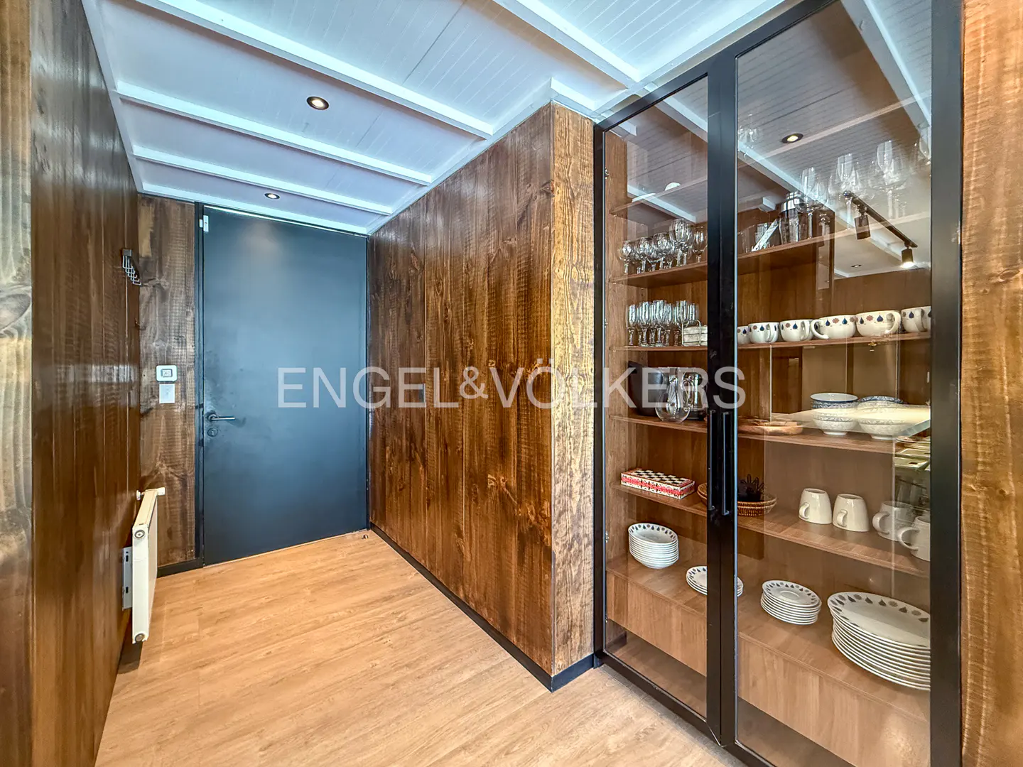 Hallway with wood paneling, a black door, and a glass cabinet filled with dishes and glassware.
