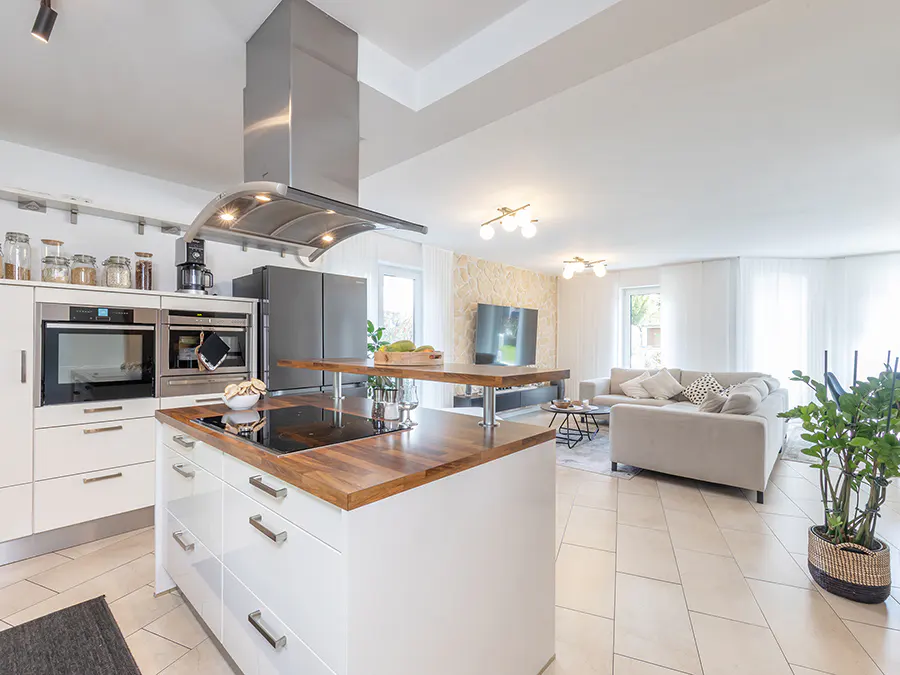 Open-concept kitchen and living room with white cabinets, wood countertops, stainless steel appliances, and a gray sofa.