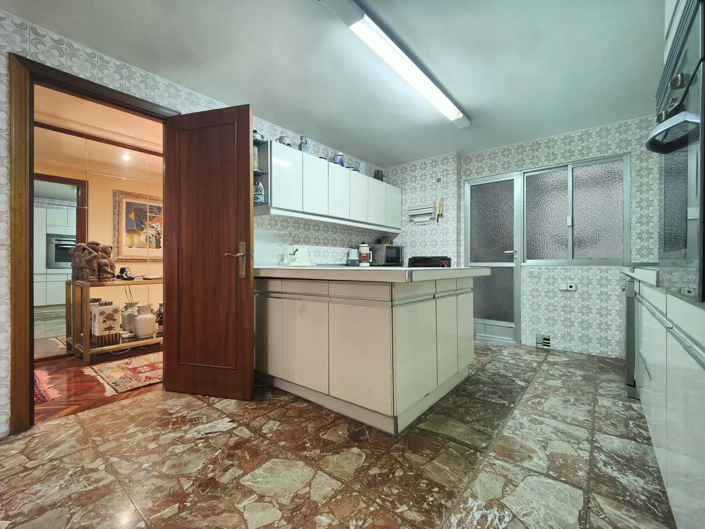 A kitchen with marble floors, white cabinets, and a brown door leading to another room.