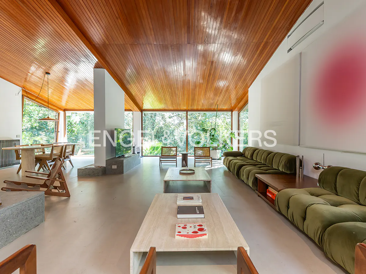 A bright living room with a wooden ceiling, large windows, a green sofa, and a dining table.