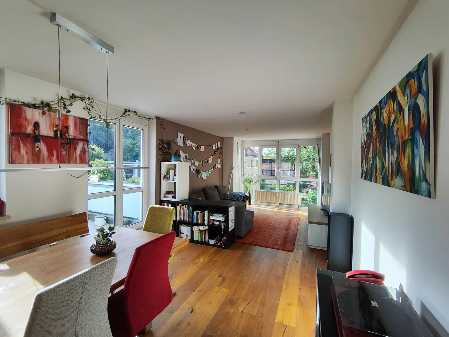 Bright, open living space with hardwood floors, a dining table with colorful chairs, and a gray sofa. Artwork adorns the walls.