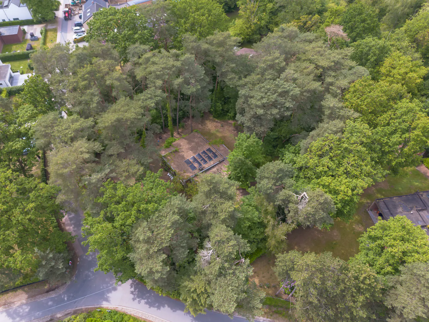 Aerial view of a house surrounded by green trees, with a road visible on the left.