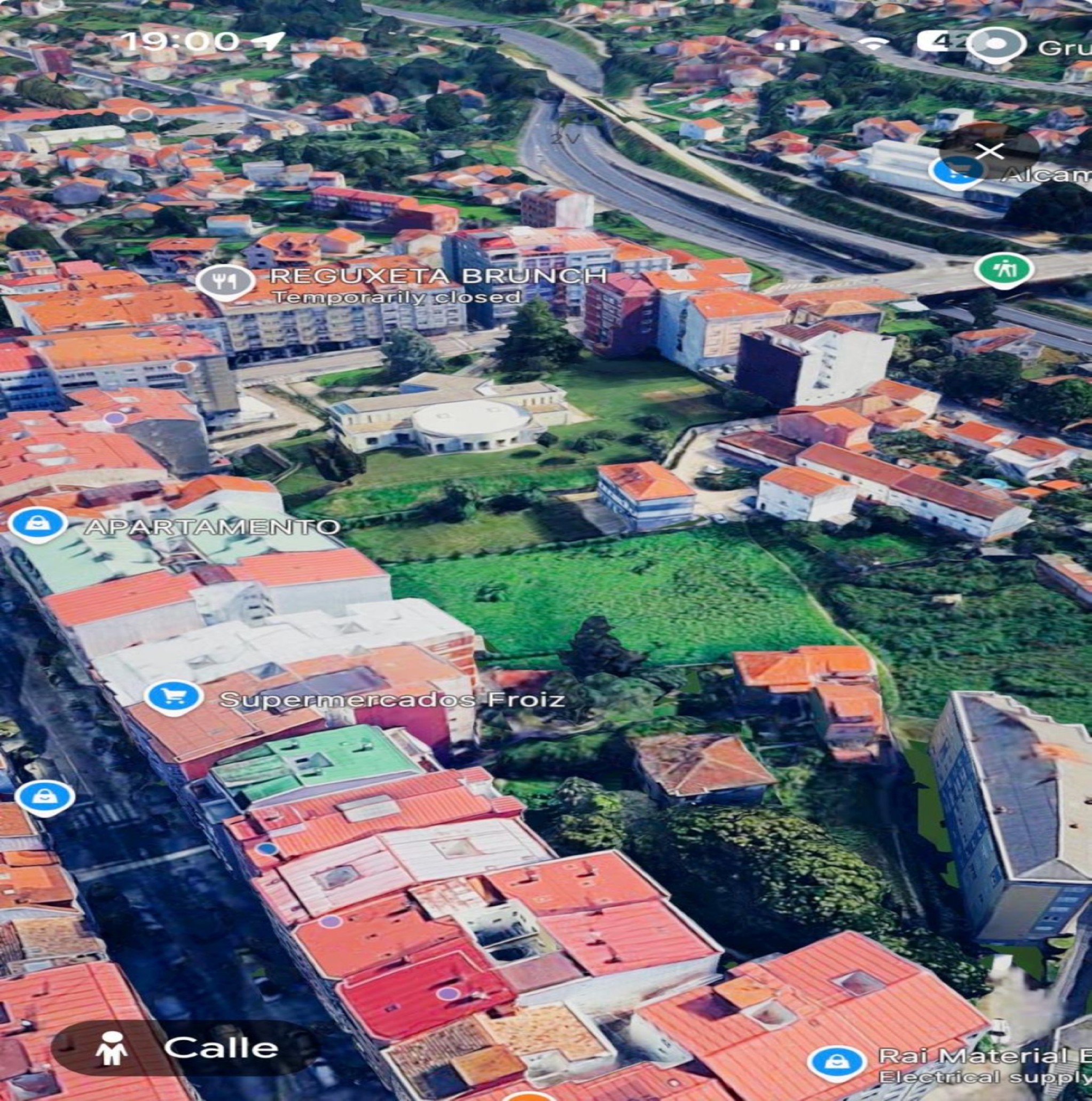 Aerial view of a neighborhood with red-roofed buildings, green spaces, and digital location markers for local businesses. [AI-generated text]