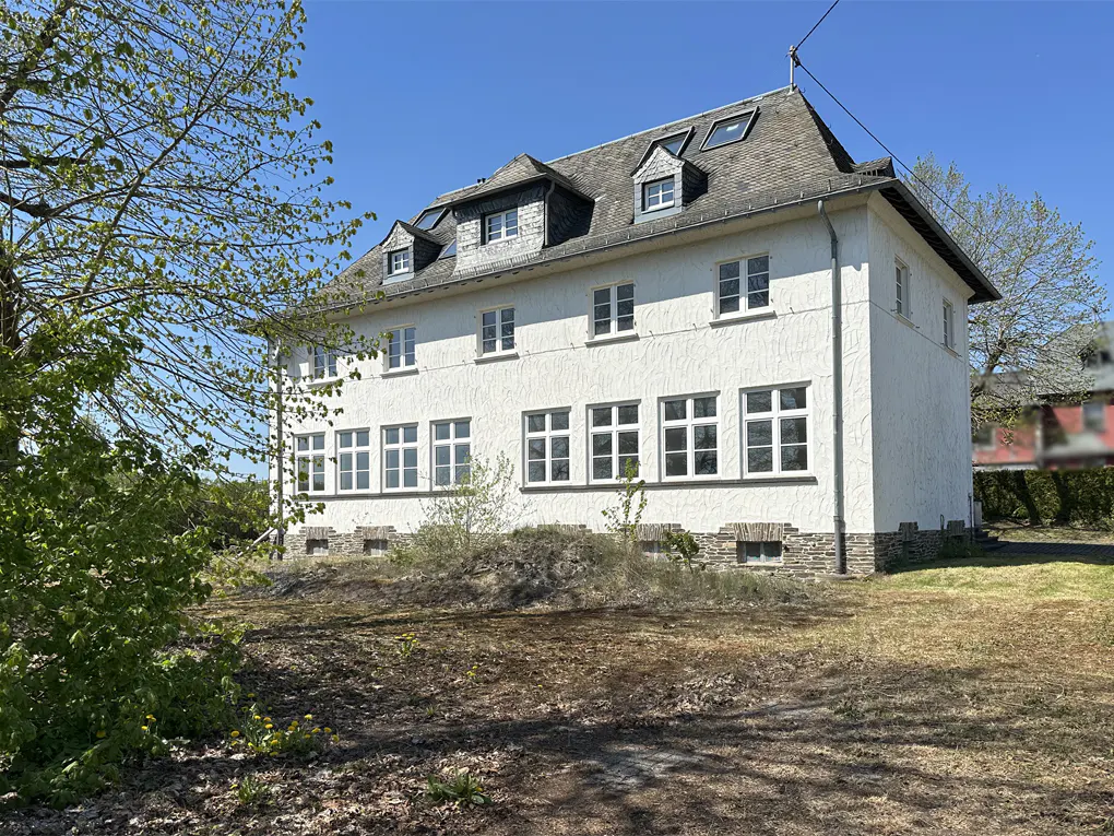 Exterior view of a three-story white house with a gray roof and many windows on a sunny day.