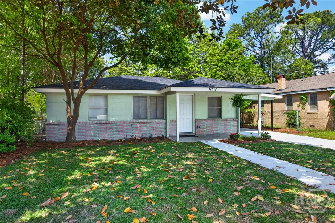 A light green single-story house with a white door and brick foundation on a grassy lawn.