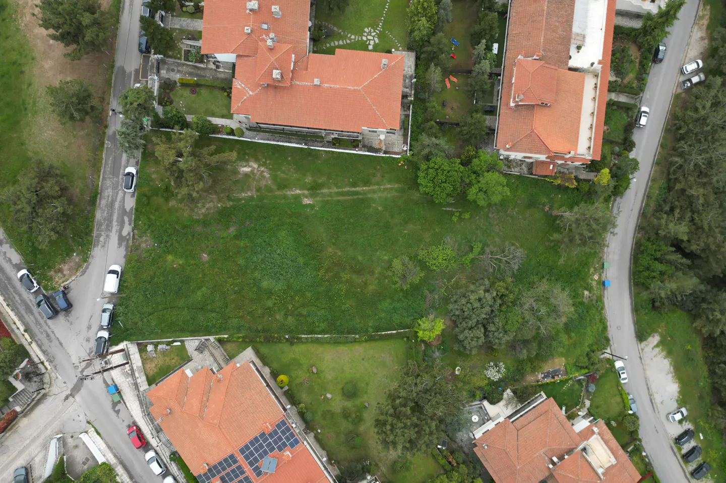 Aerial view of a large, grassy lot surrounded by houses with red tile roofs and streets with parked cars.