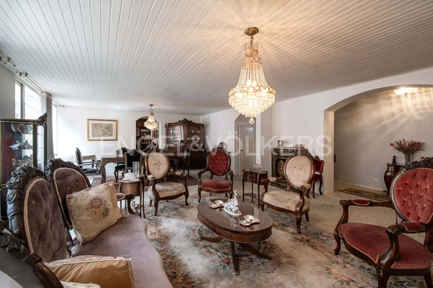 Ornate living room with antique furniture, including a crystal chandelier, chairs, and a floral rug.