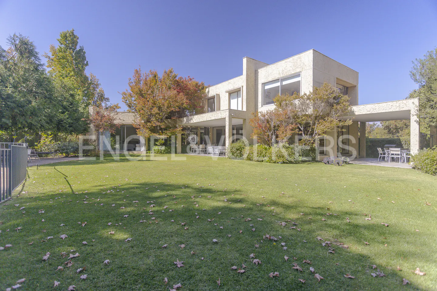 Two-story beige house with a large green lawn and trees under a blue sky.