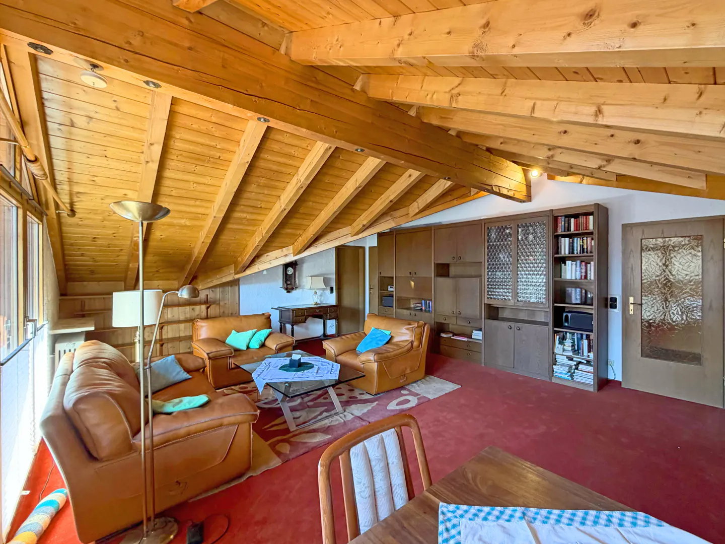 Attic living room with wood-beamed ceiling, red carpet, brown leather furniture, and built-in wooden cabinets.