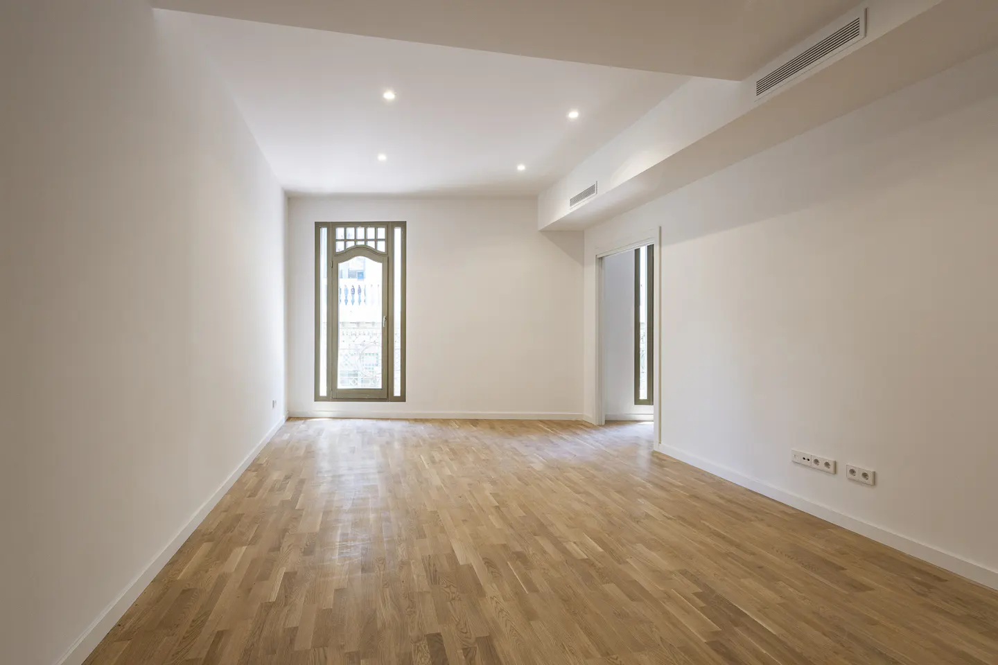 Bright, empty room with hardwood floors, white walls, and a decorative window.