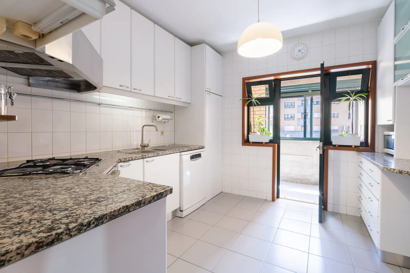 Bright kitchen with white cabinets, granite countertops, and tiled floor. A door leads to a balcony with plants.