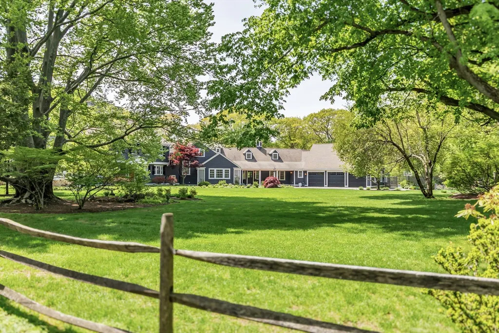 A gray house with a green lawn is framed by a wooden fence and trees.