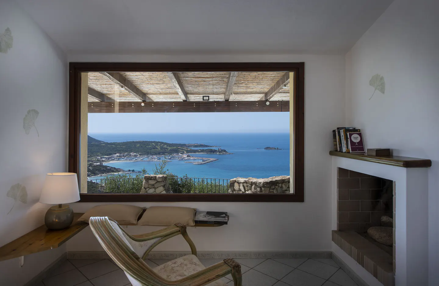Living room with a view of the ocean. A chair sits near a window overlooking a harbor and turquoise water. A fireplace is on the right.