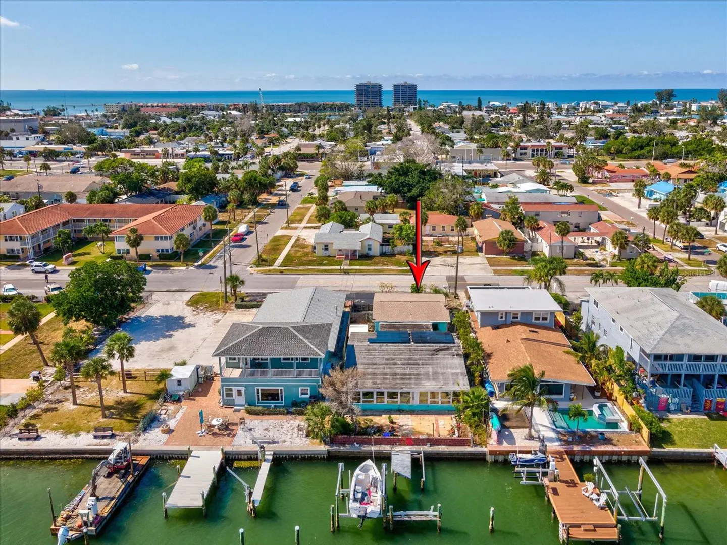 Aerial view of waterfront homes with docks and boats on a sunny day. An arrow points to a house in the neighborhood.