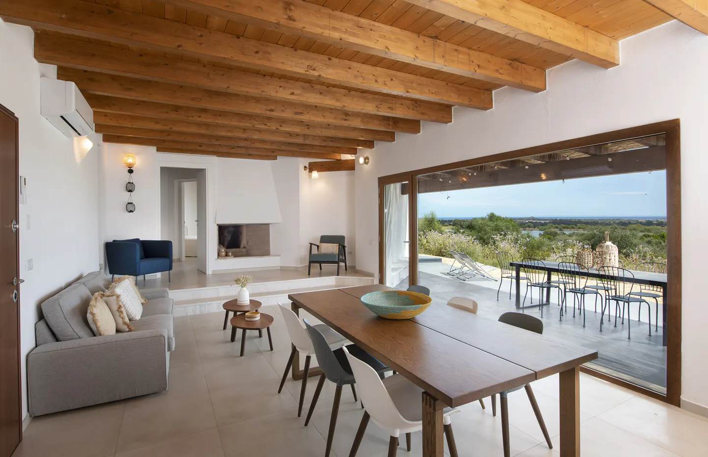 Bright living room with wood-beamed ceiling, fireplace, and large sliding glass doors to a patio with a view.